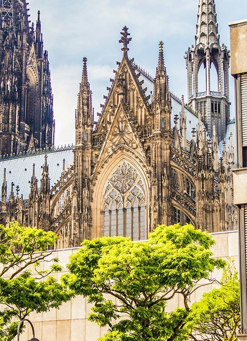 Gothic cathedral façade with intricate spires, stone arches, and green trees in the foreground.
