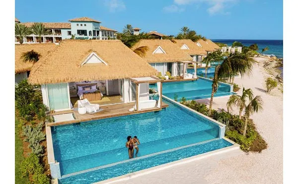 Luxury resort with bungalows, infinity pools, and a couple in the water near a beach.