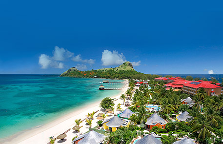 Tropical beach resort with turquoise water, white sand, and lush green vegetation.