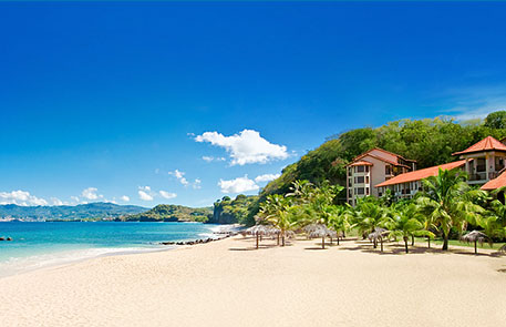 Beach scene with sandy shore, turquoise water, blue sky, and a resort building.