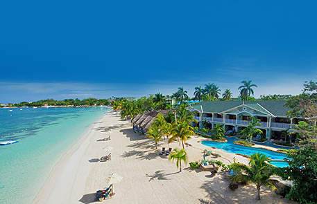 Beachfront resort with white sand, turquoise water, palm trees, and a pool under a clear blue sky.