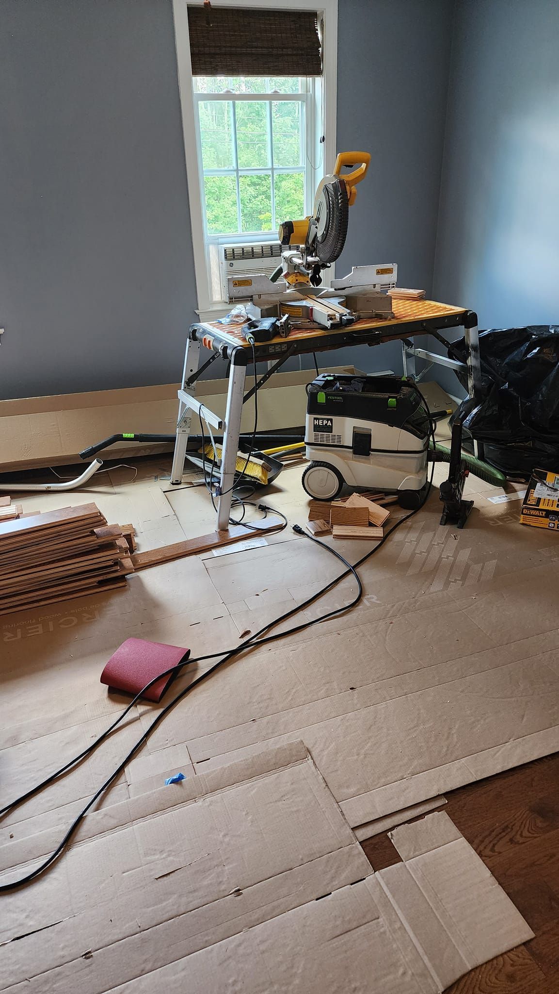 Room with power tools, including a miter saw on a stand, and flooring installation in progress.