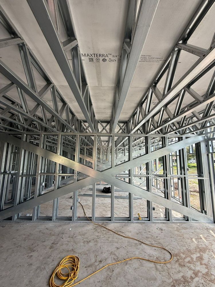 Interior construction site with exposed ceiling framing, hanging wires, and unfinished metal wall studs