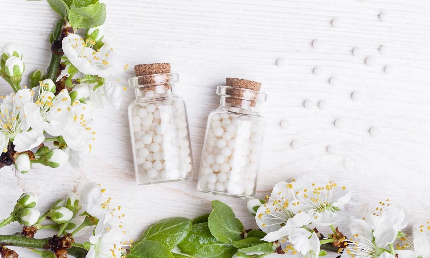 Dos frascos de pastillas de homeopatía y flores sobre una mesa blanca.