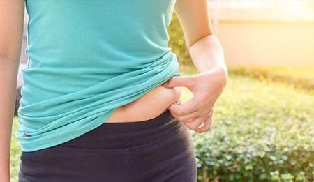 Una mujer con una camisa azul y pantalones negros se sostiene el estómago.