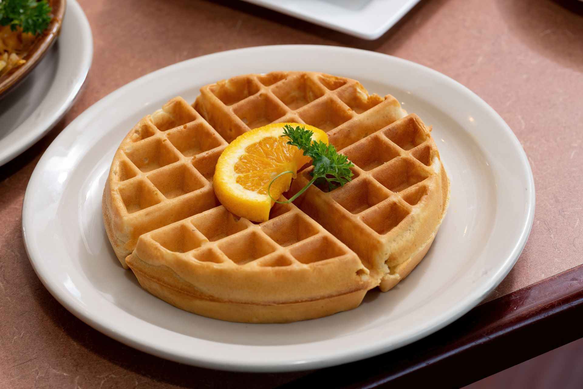 A waffle with a slice of orange on top on a white plate.