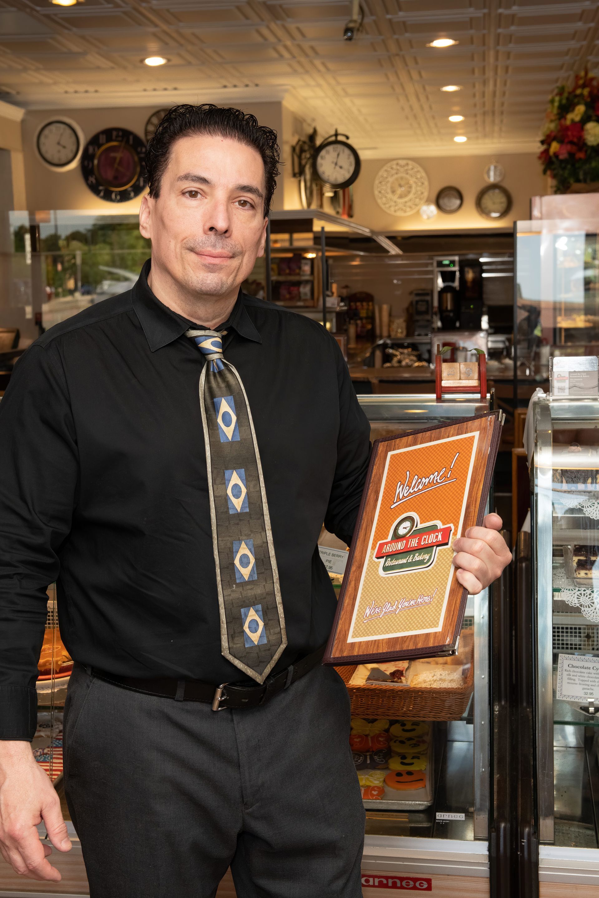 A man in a black shirt and tie is holding a menu