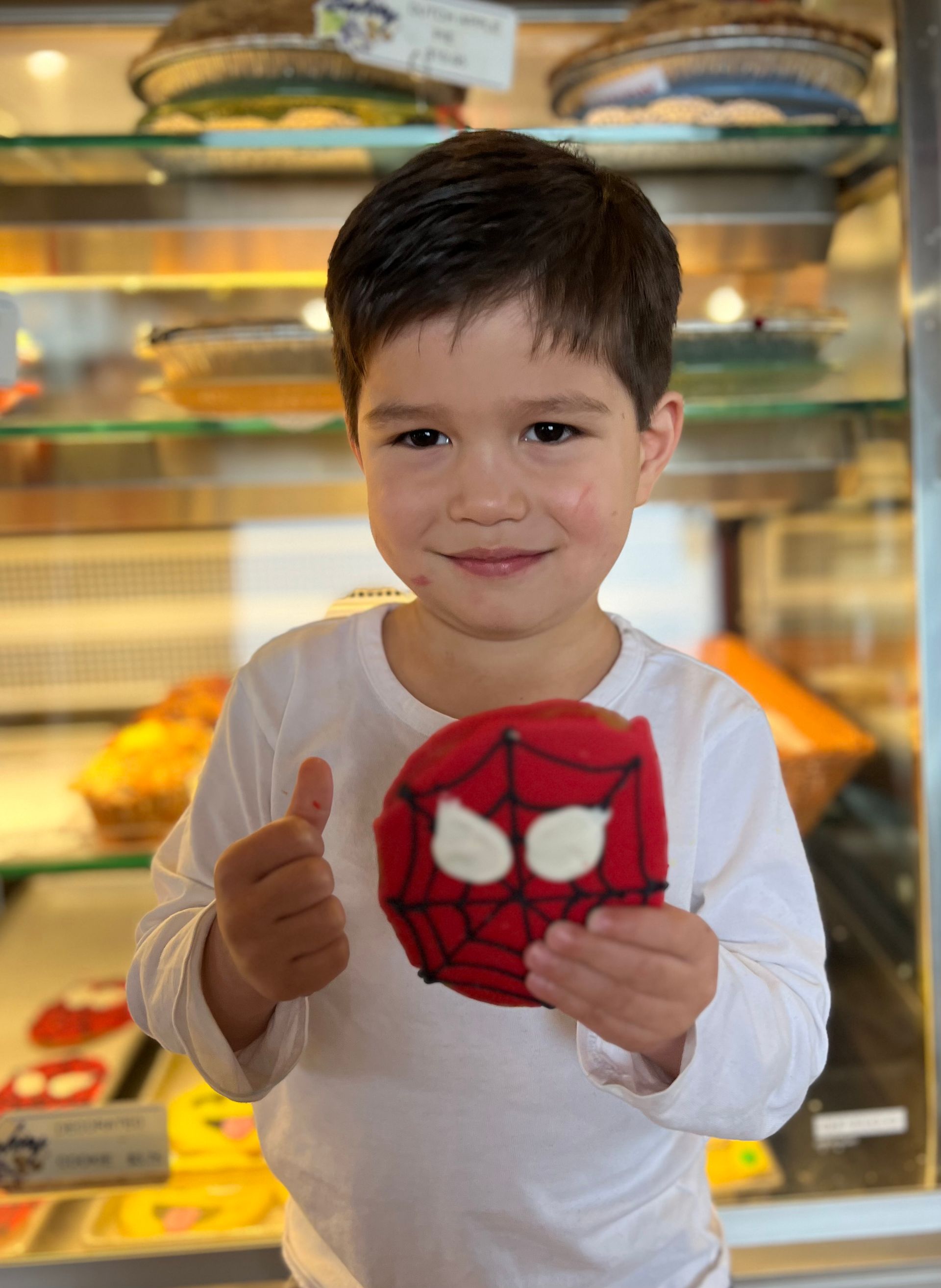 A young boy is holding a spiderman cookie and giving a thumbs up.