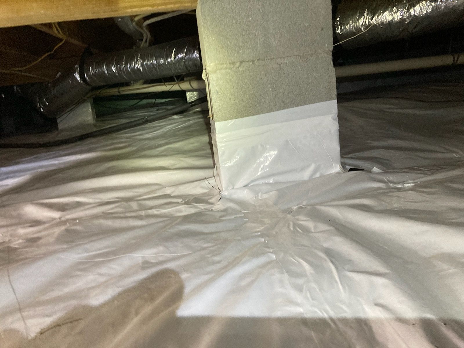 Insulated crawlspace with ductwork and a white plastic vapor barrier on the floor and support post