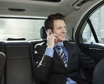 Un homme en costume et cravate est assis sur le siège arrière d'une voiture et parle sur son téléphone portable.