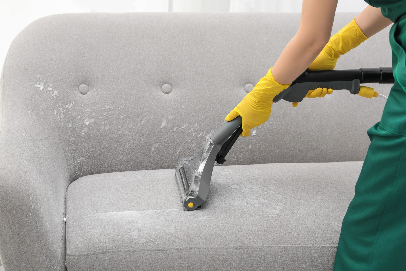 A woman is cleaning a couch with a vacuum cleaner.