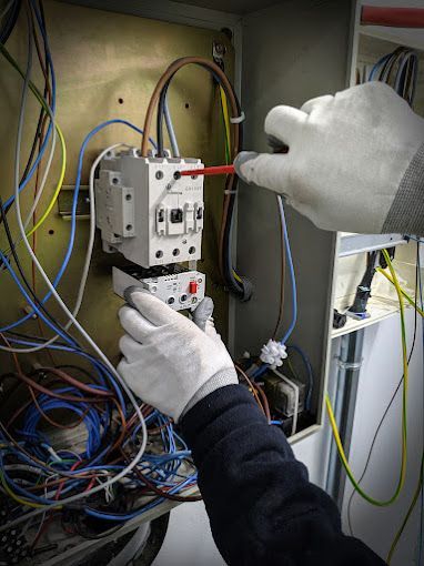 A person is working on an electrical box with a screwdriver.