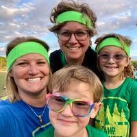 Four smiling people wearing green headbands and shirts pose outdoors under a cloudy sky.