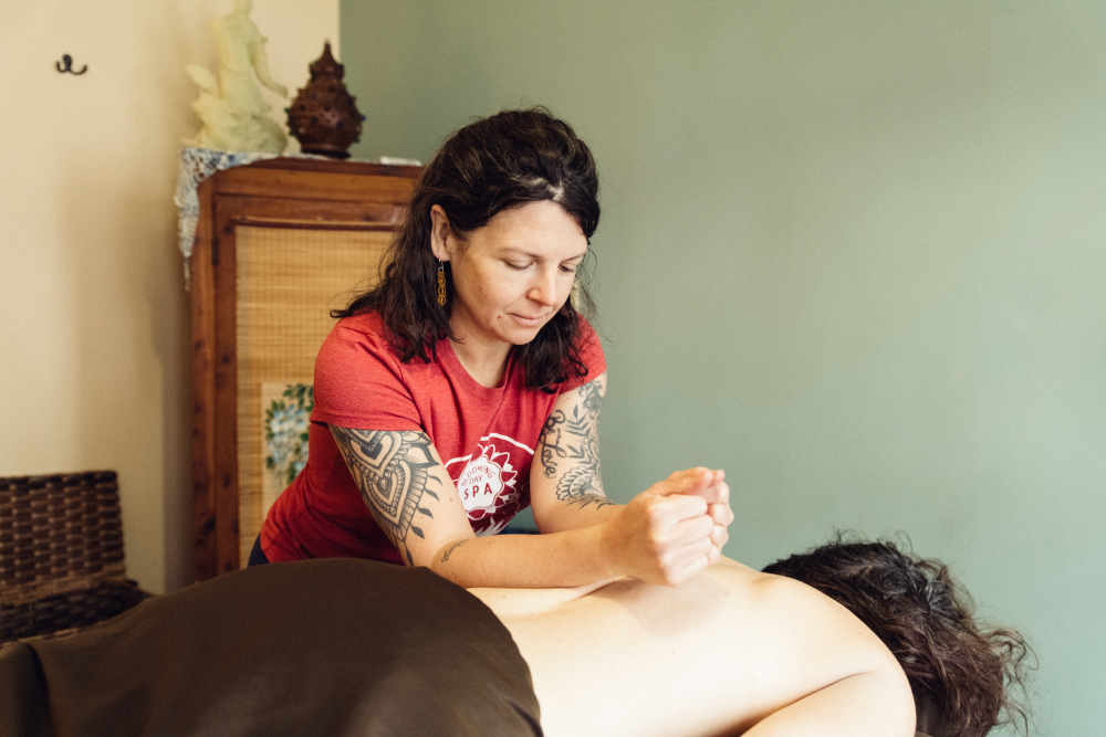 Woman in red shirt giving a massage on a bed in a softly lit room