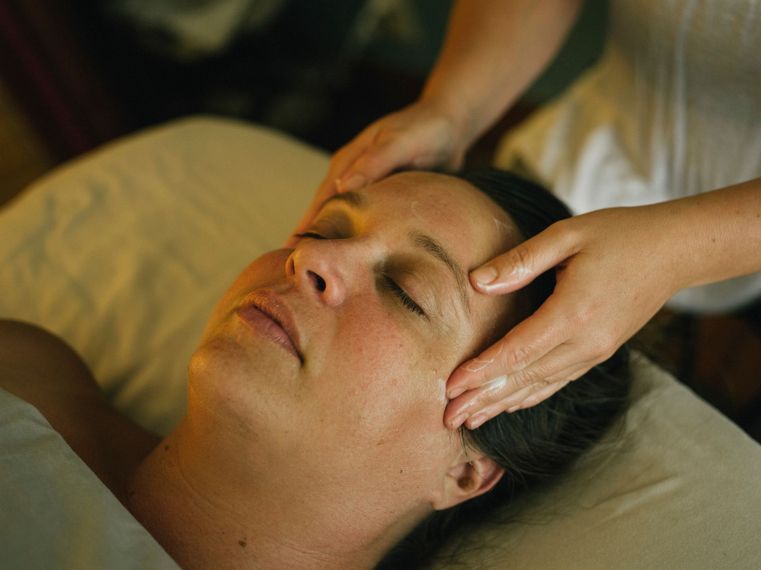 Hands giving a facial massage to a relaxed person lying on a treatment bed