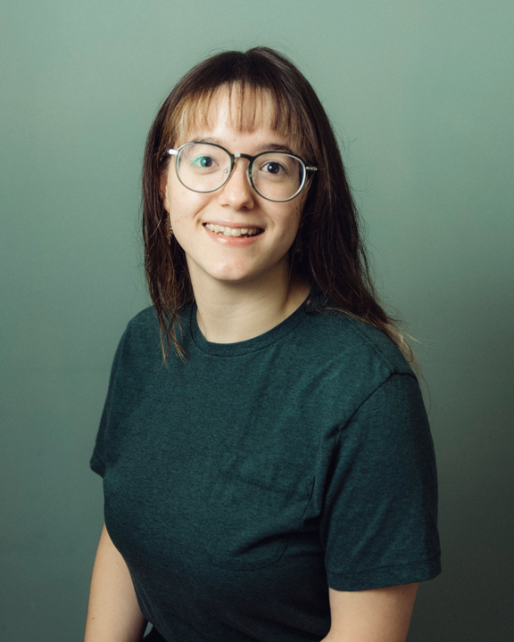 Smiling person with glasses in a dark green shirt against a muted green background