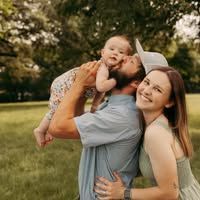 A family hugging outdoors in a grassy field, smiling under warm sunlight.