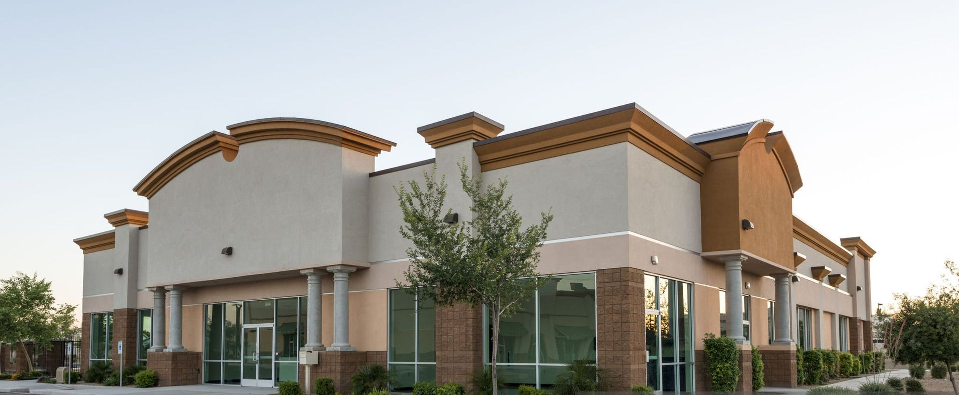 White stucco storefronts with stone columns under a clear blue sky.