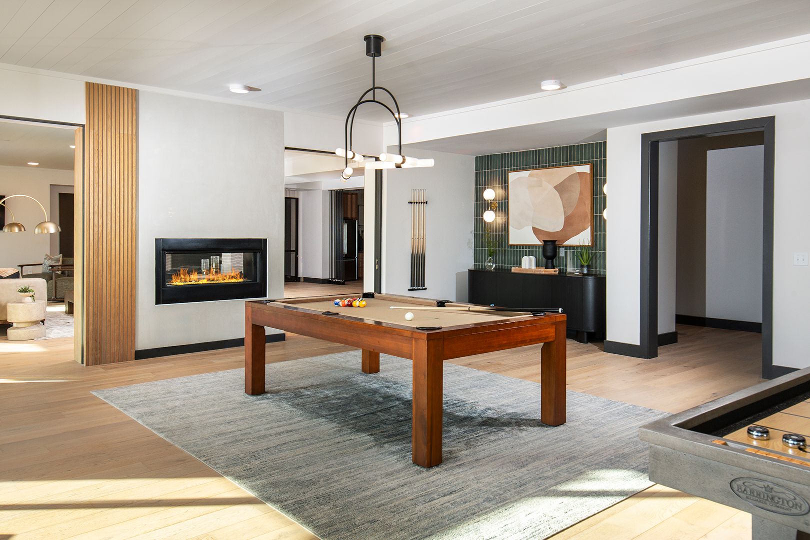Pool table in a modern game room with fireplace, rug, and decorative lighting.