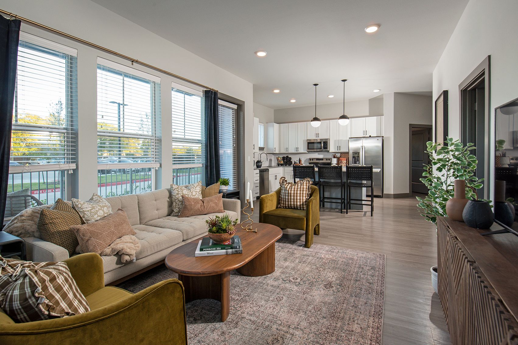 Living room with sofa, armchairs, coffee table, rug, and kitchen in background.