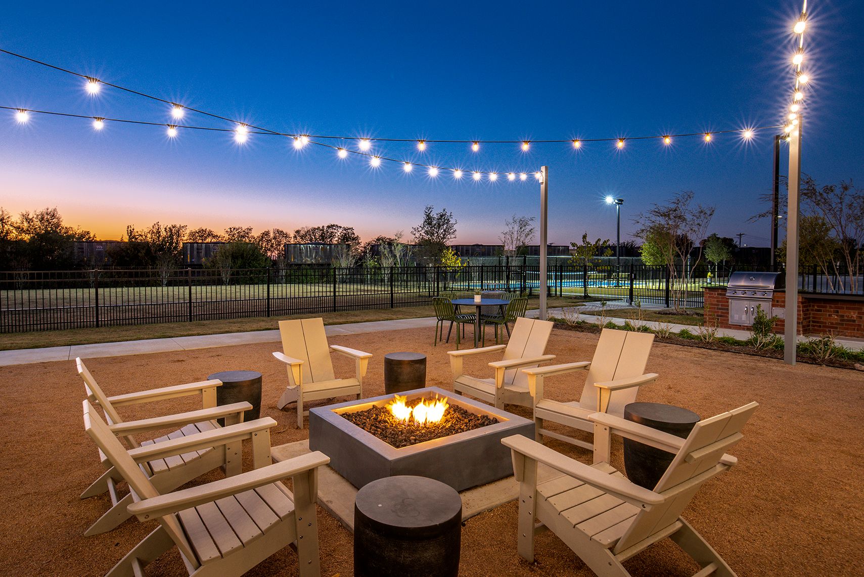 Outdoor seating area with fire pit, string lights, and chairs, at dusk.