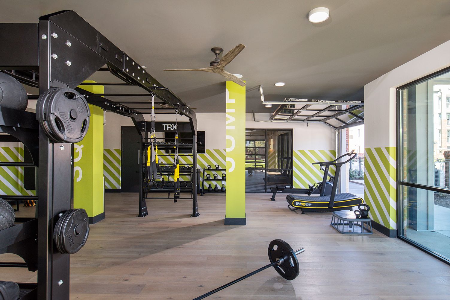 Gym interior with weight rack, pull-up bars, weights, and cardio machines. Bright green and yellow accents.