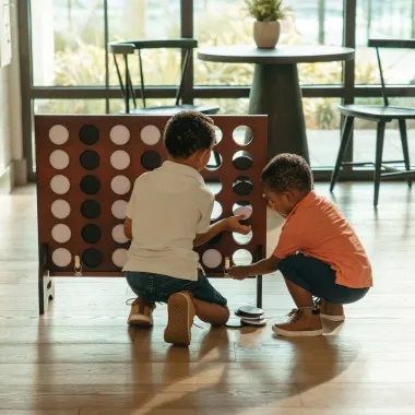 Two young boys are playing a game of connect four on the floor.