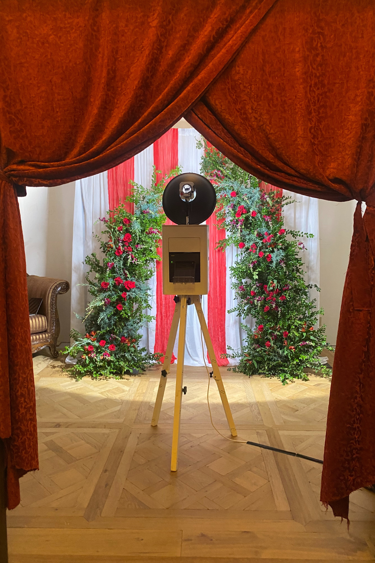 Photo booth with tripod camera framed by red curtains in a decorated room
