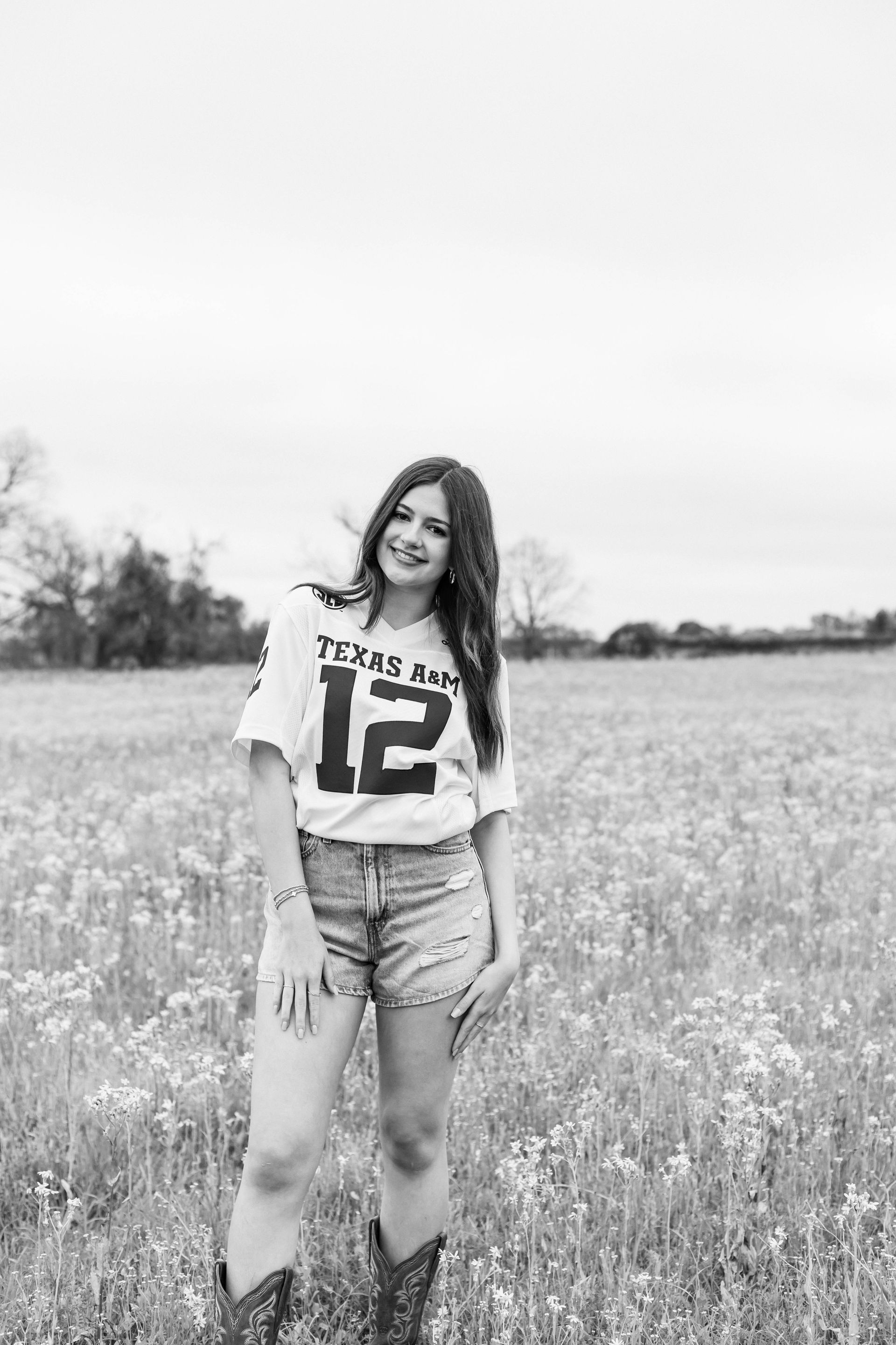 Person standing in a grassy field, smiling, wearing a white jersey and shorts.