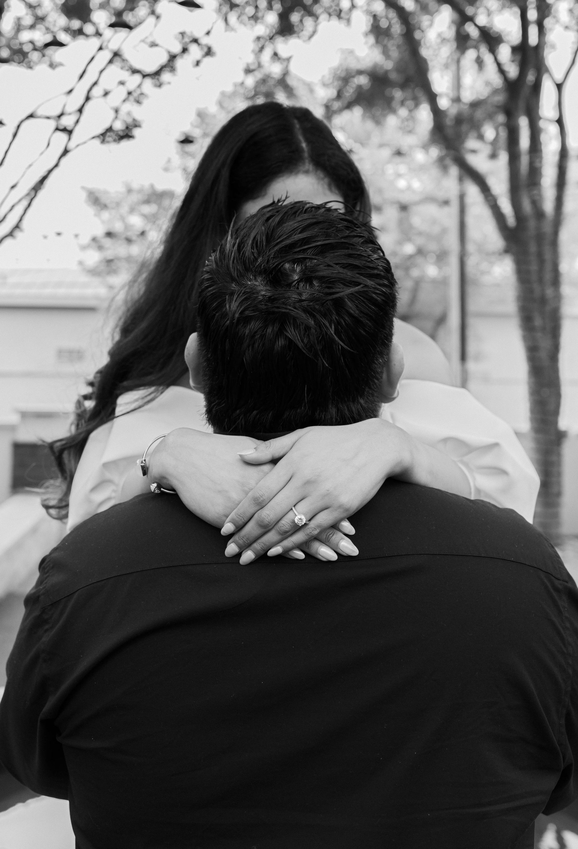 Couple embracing outdoors, black-and-white portrait with trees in the background