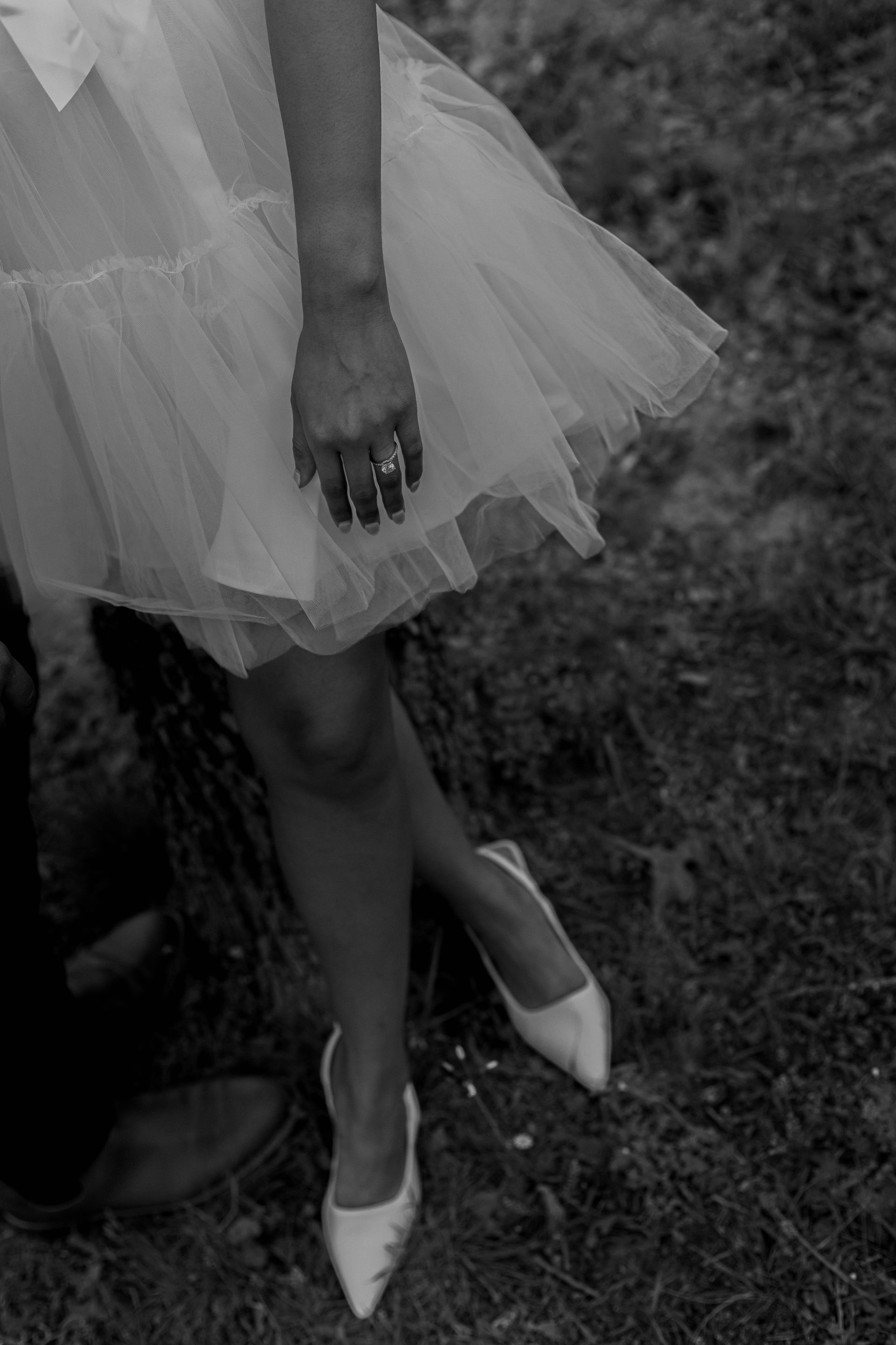 Person in a white tulle dress and heels standing on grass, holding a bouquet.