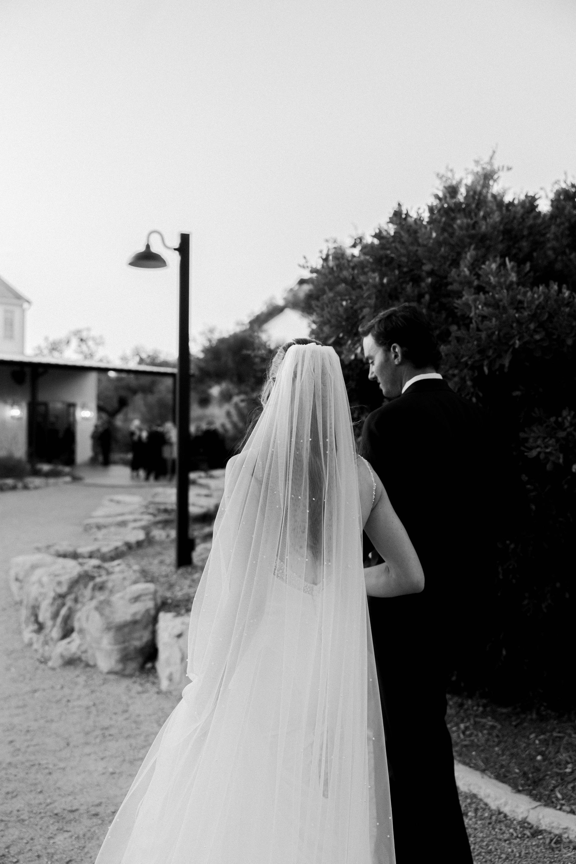 Bride and groom walking outdoors near a lamppost, bride in a long veil and gown