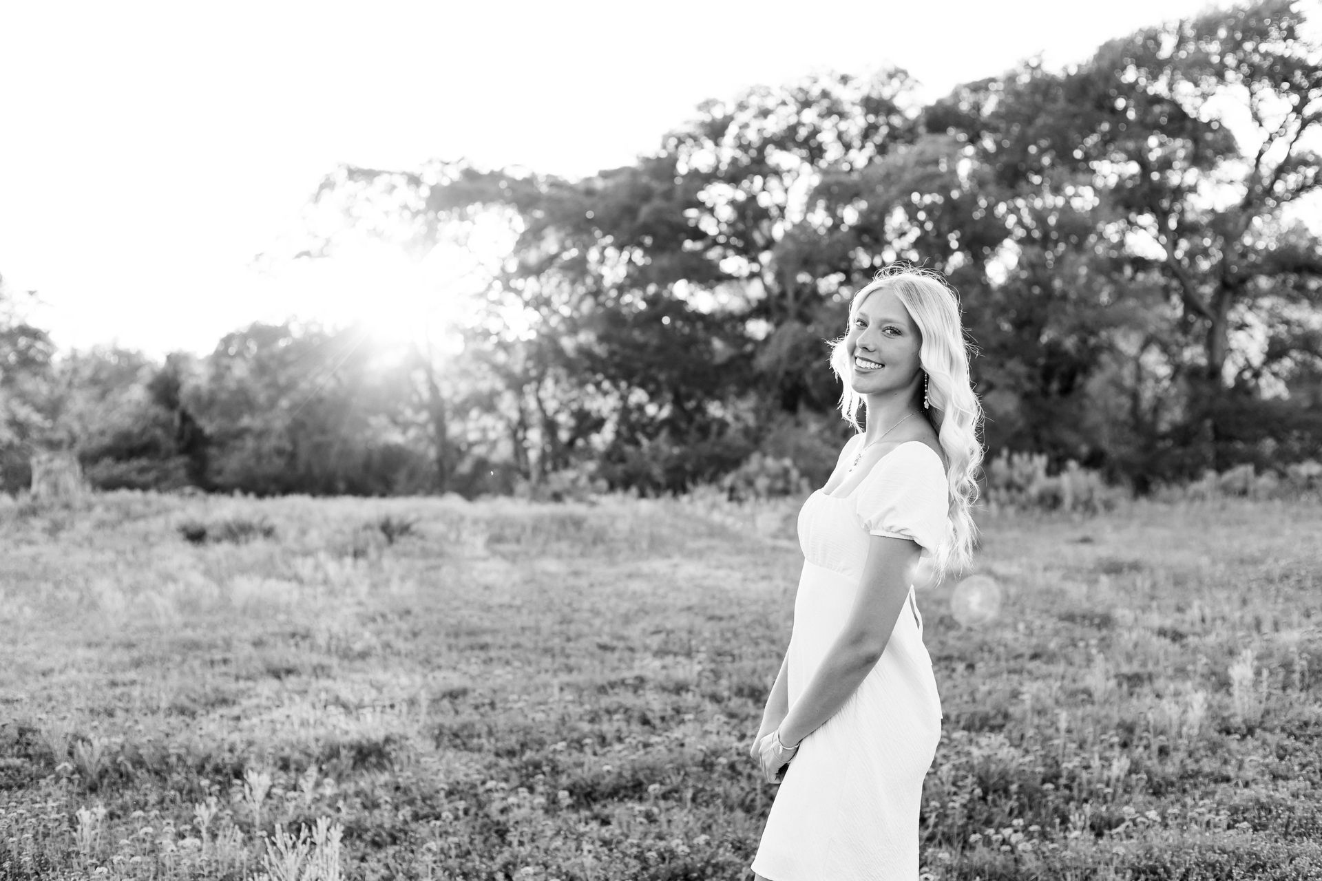 Smiling woman in a white dress standing in a grassy field at sunset