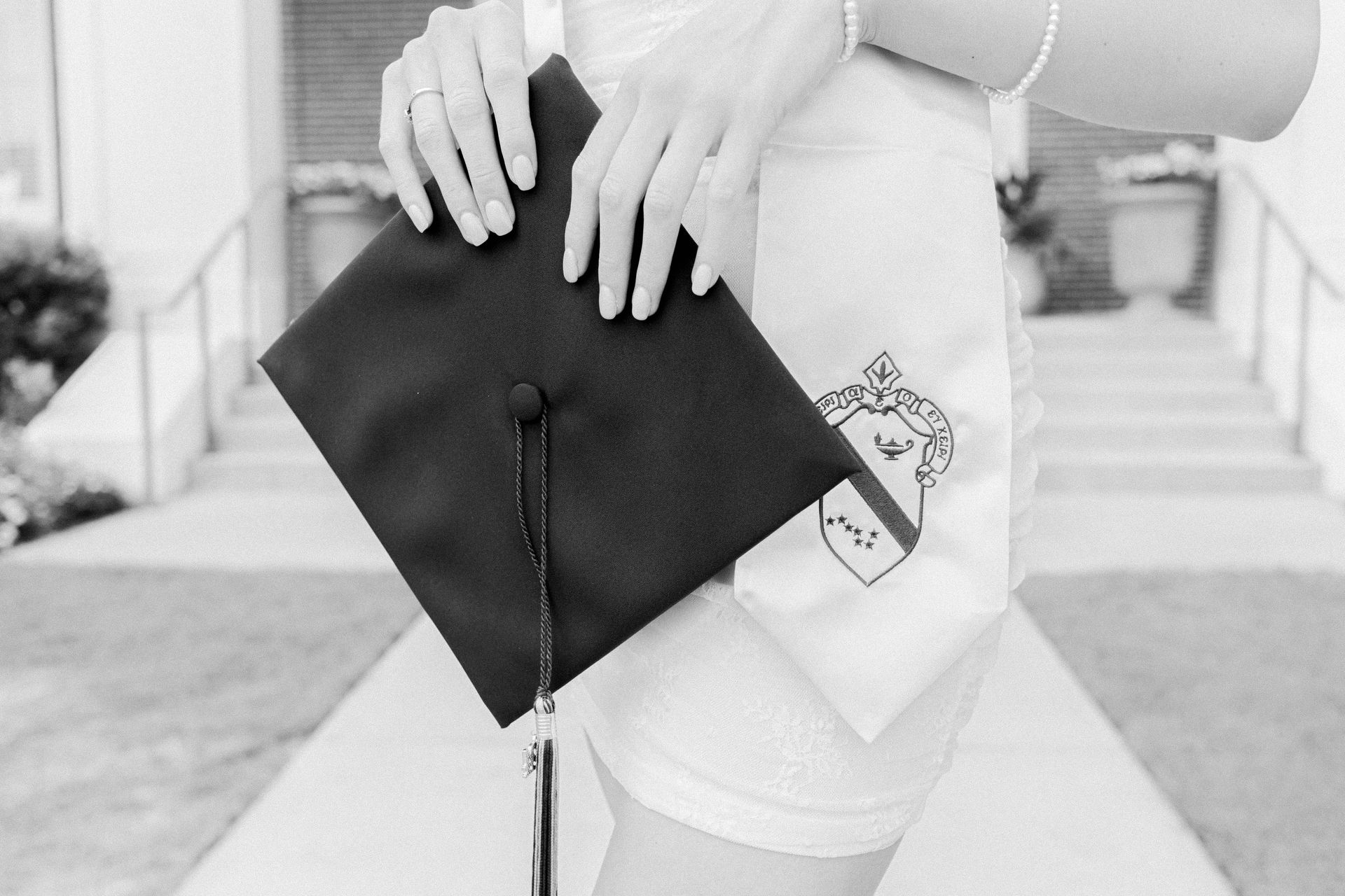 Person holding a black graduation cap in front of a building with steps