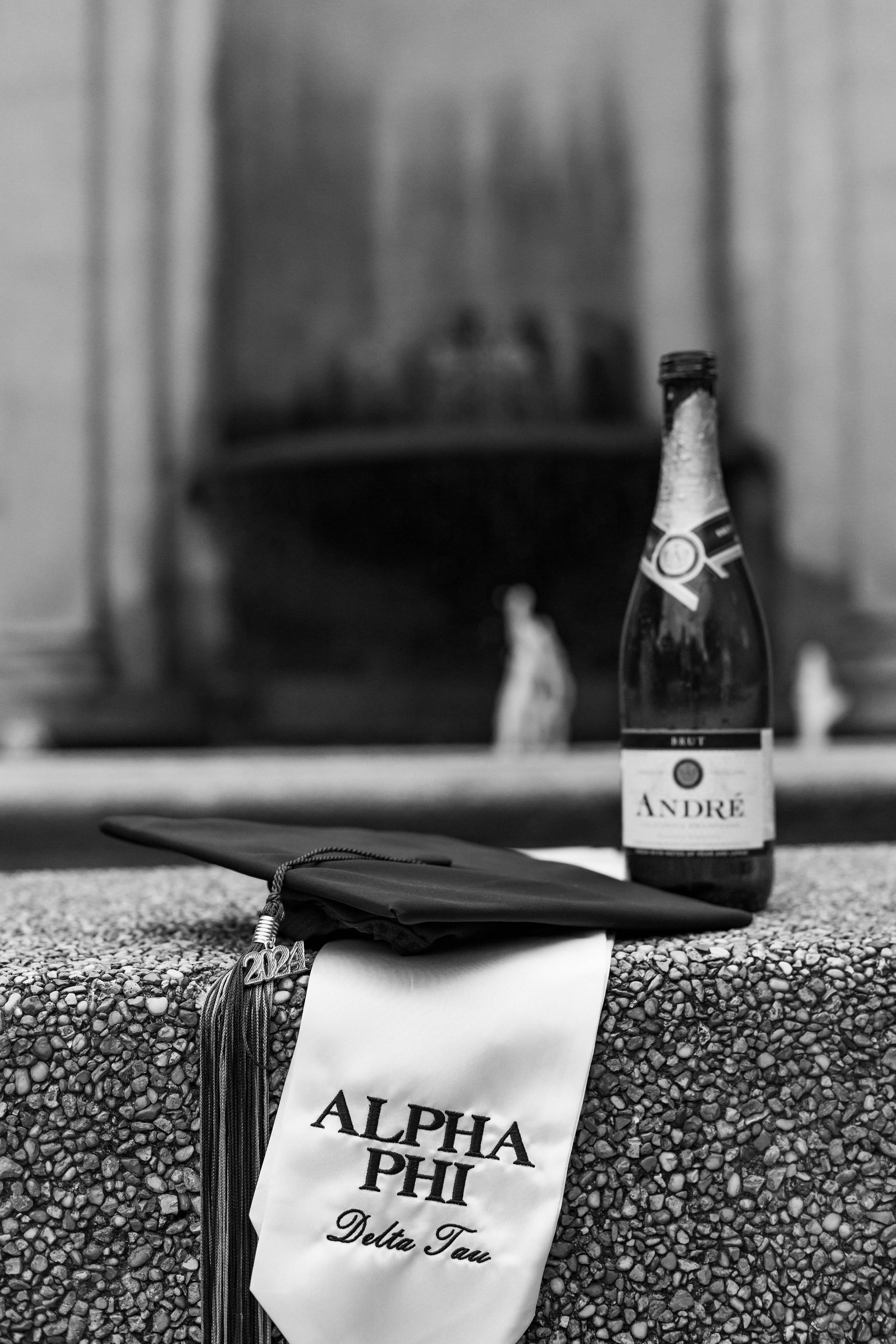 Black-and-white gift bag and wallet beside a champagne bottle on a table, with a blurred fireplace behind.
