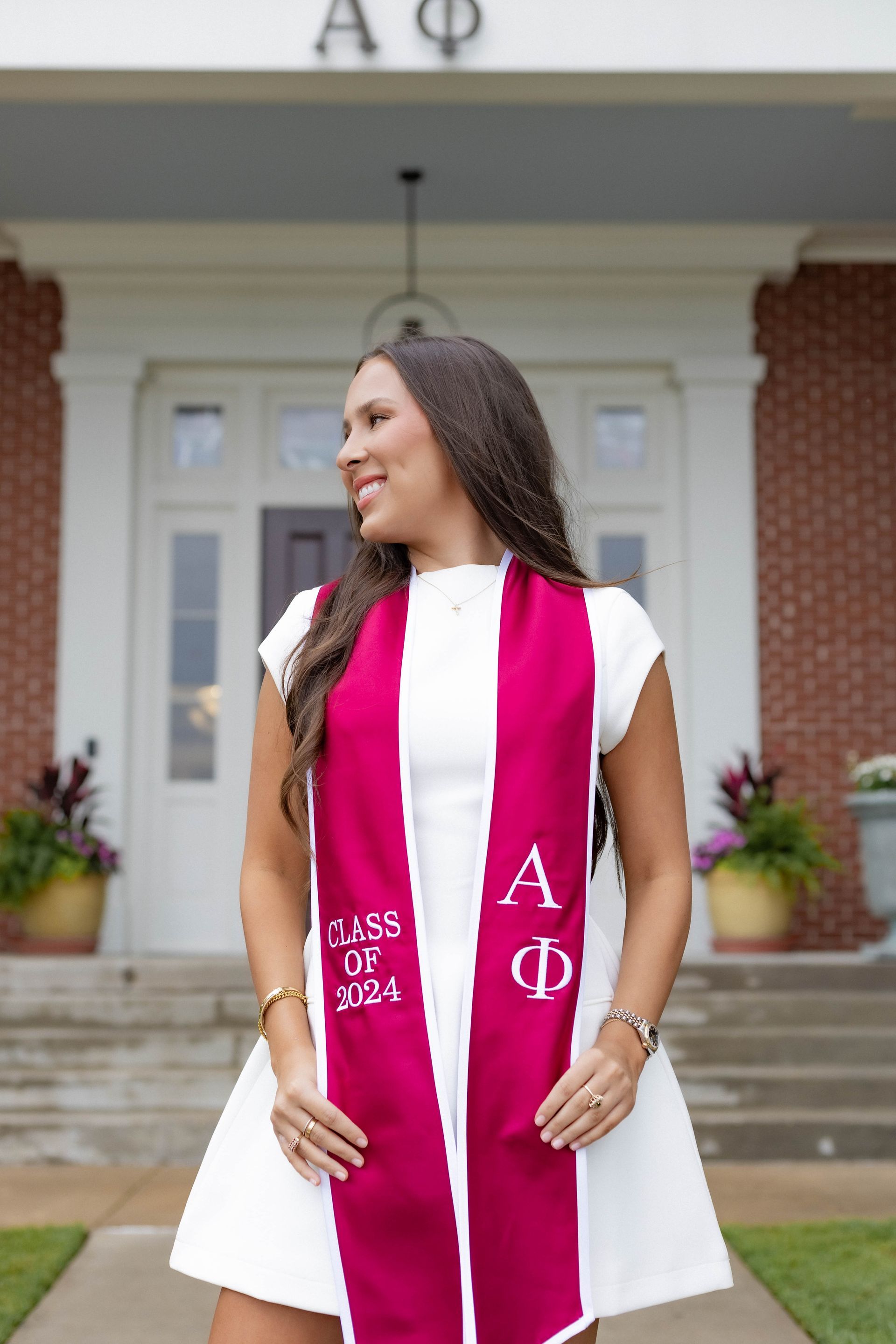 Person in white dress and magenta stole stands on steps outside a building, looking to the side.