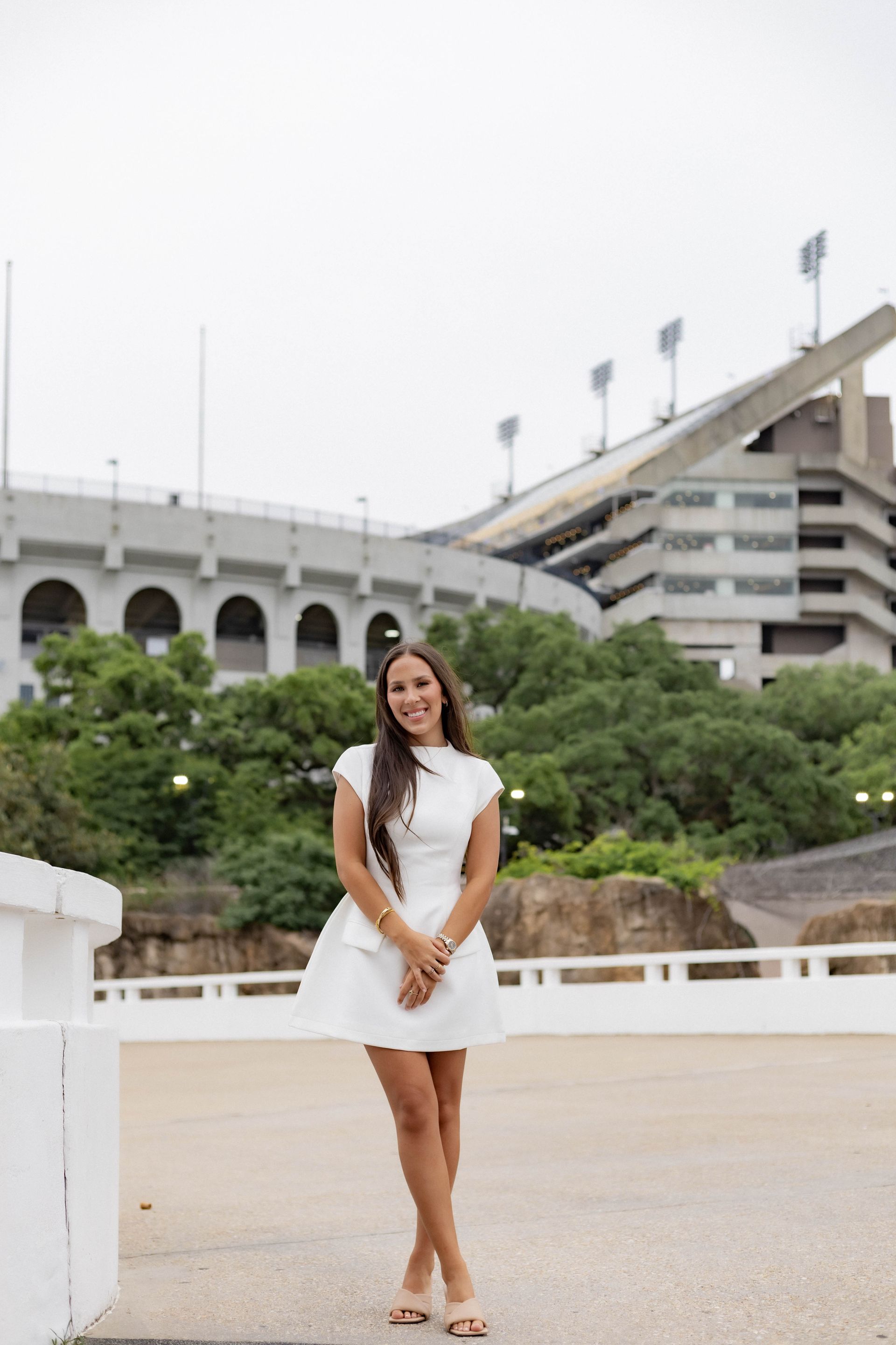 Woman in a white dress standing on a waterfront promenade with stadium seating in the background