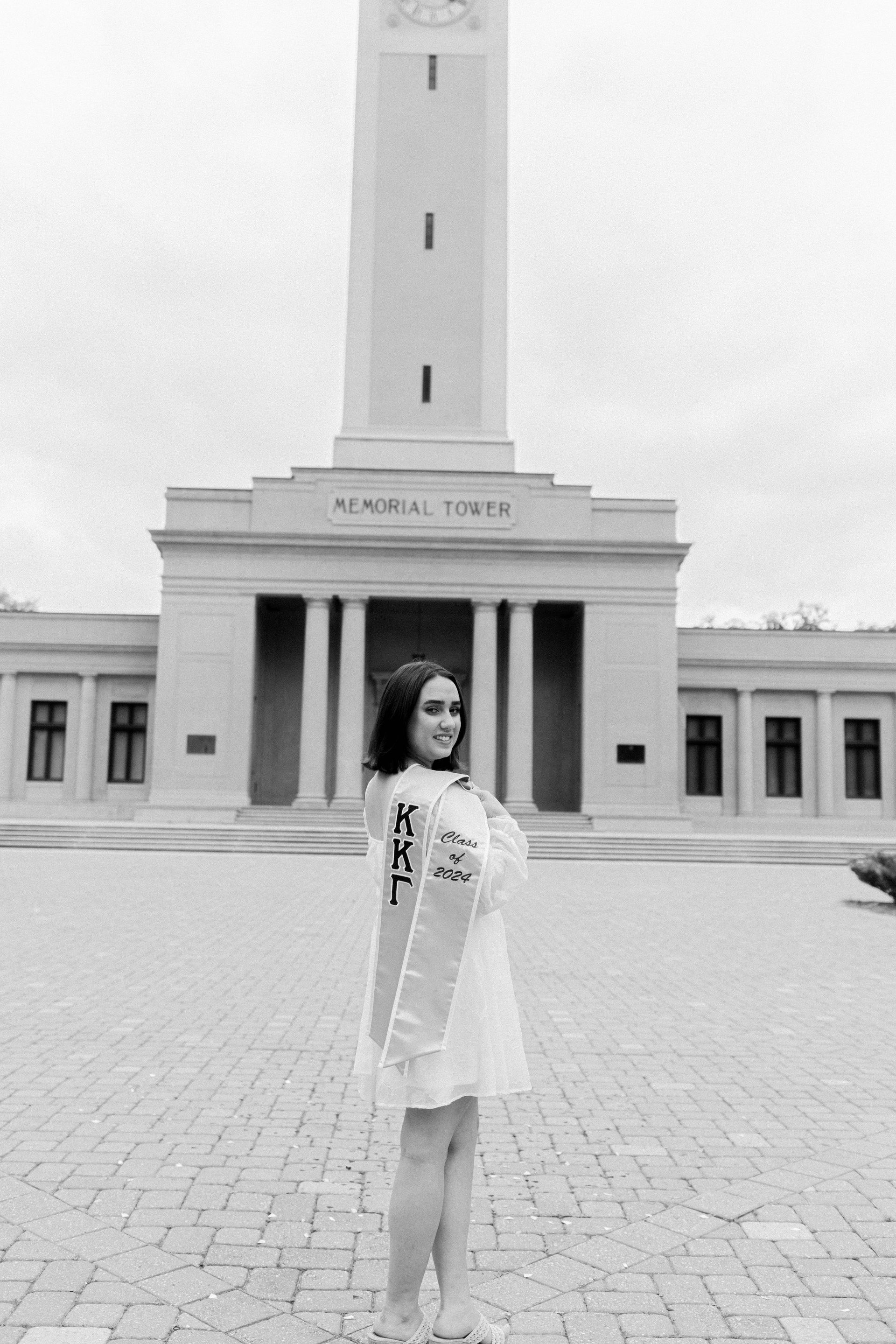 Woman in a light dress standing before a tall monument and building in a courtyard