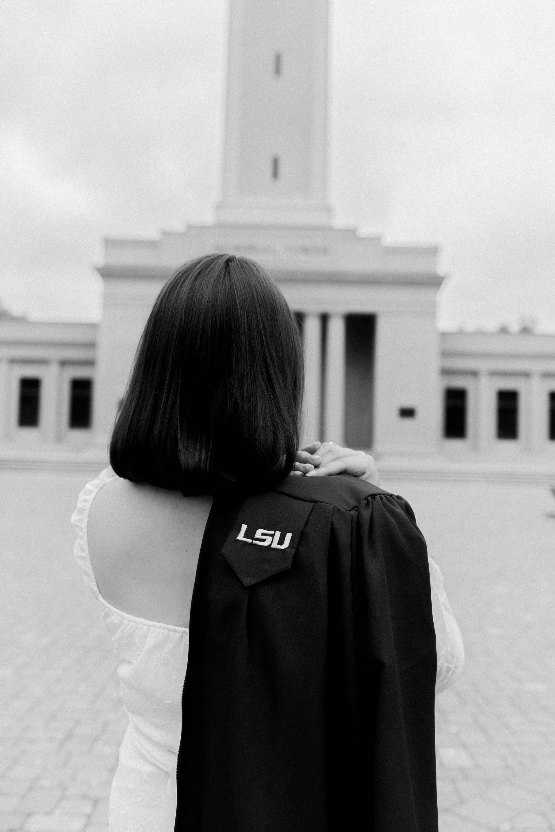 Person seen from behind, wearing a white dress and black jacket, facing a tall white monument.