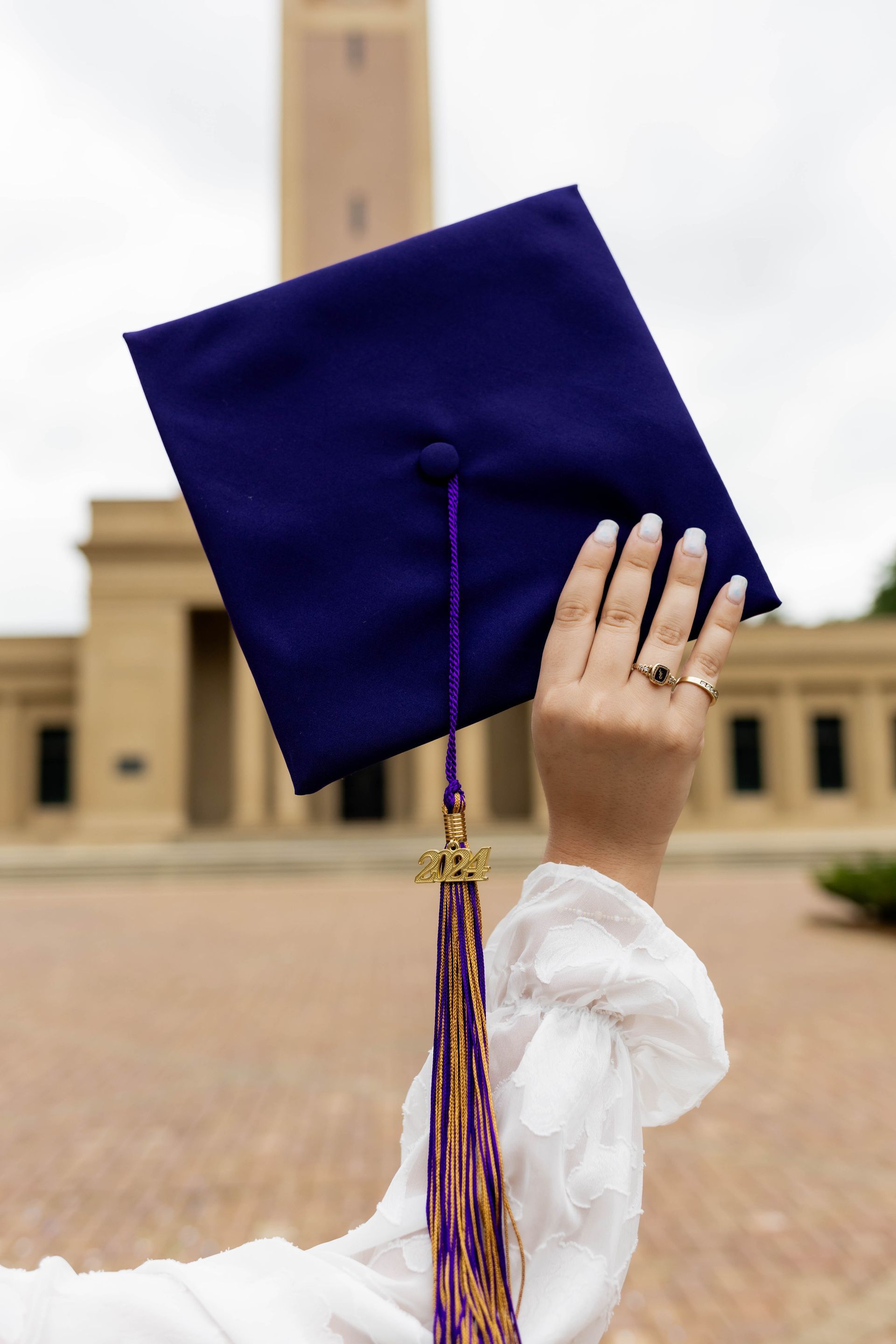 Purple graduation cap held up in front of a campus building