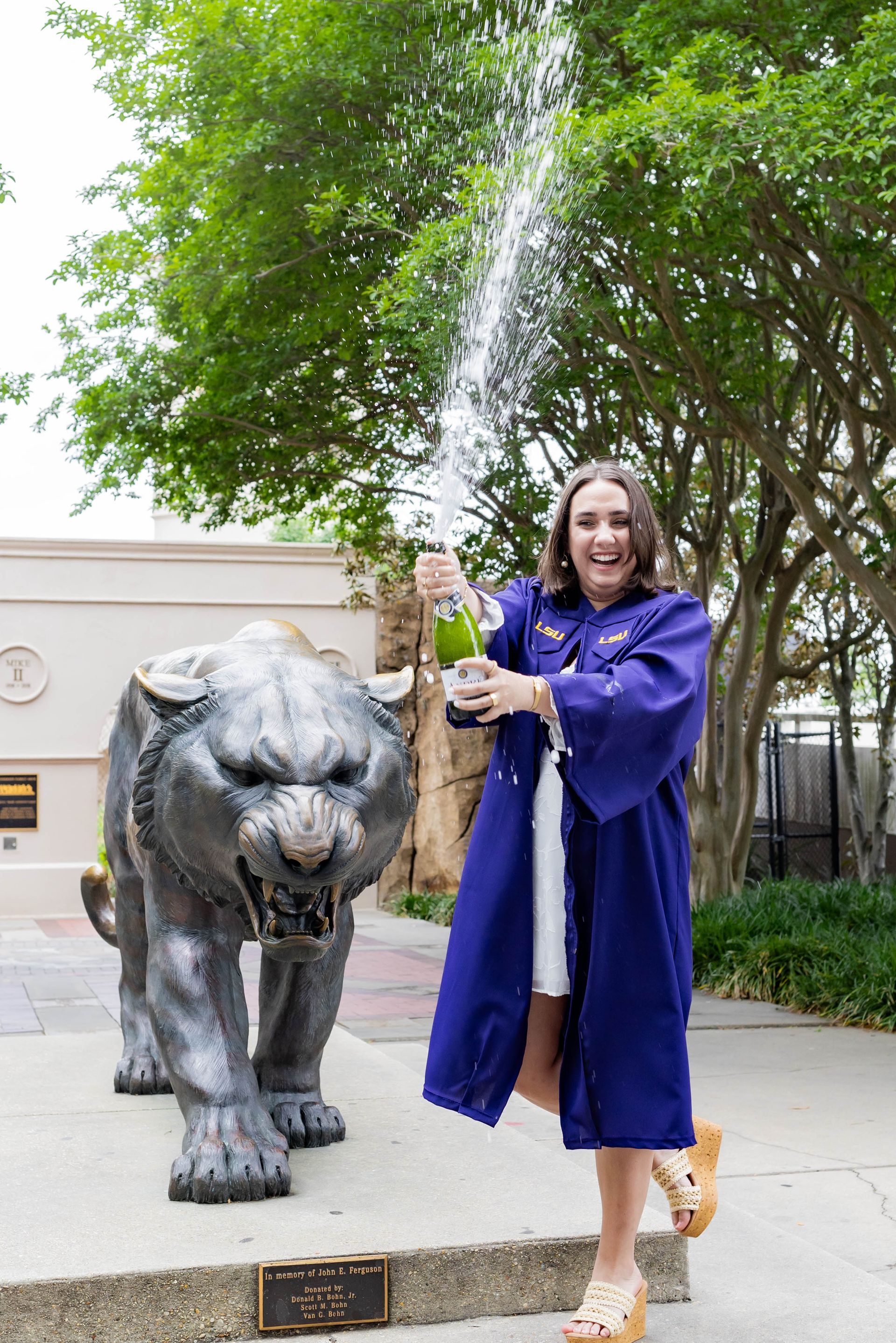 Woman in a purple robe poses beside a large bull statue outdoors under trees.