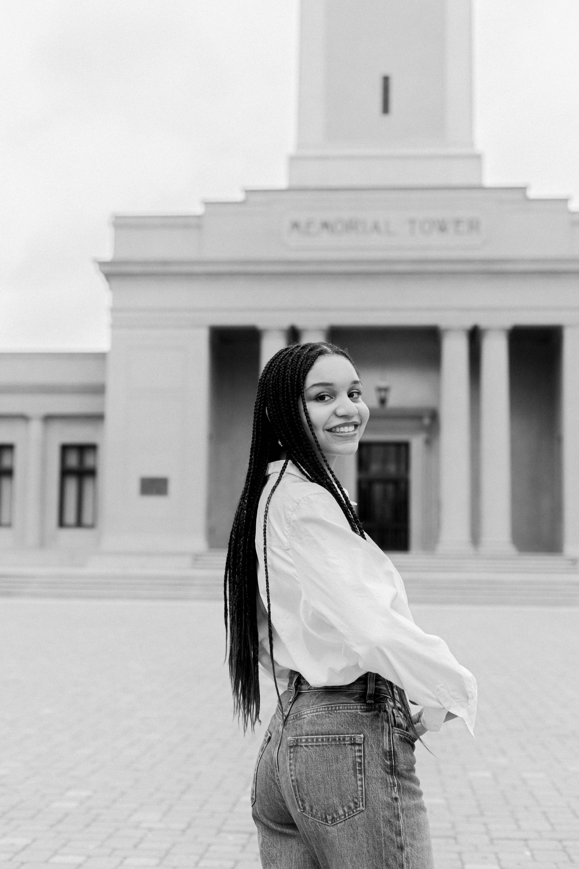Smiling woman in a white blouse and jeans standing before a memorial tower