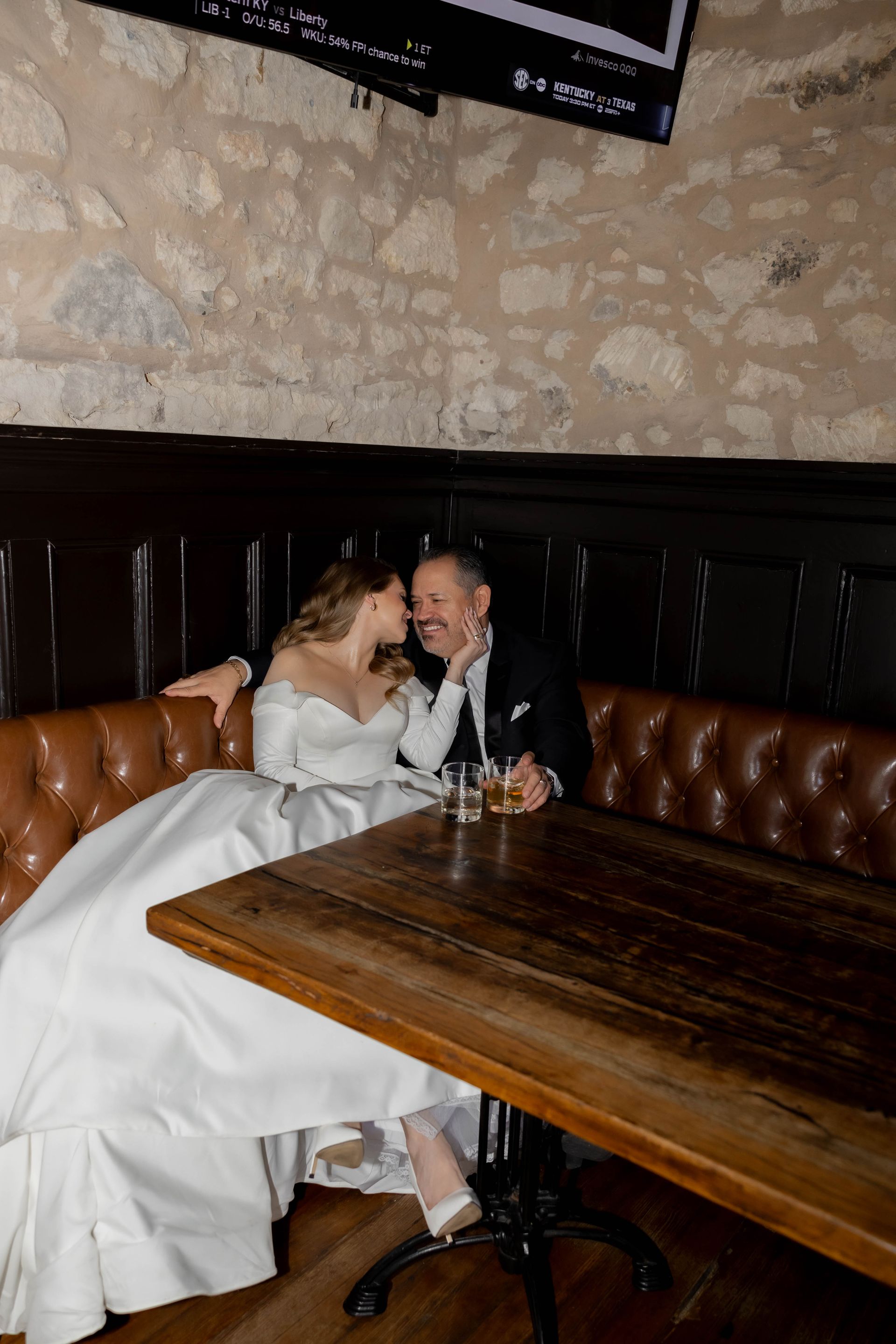 Two people in formal wear sitting in a booth at a dark wood restaurant table, leaning close together