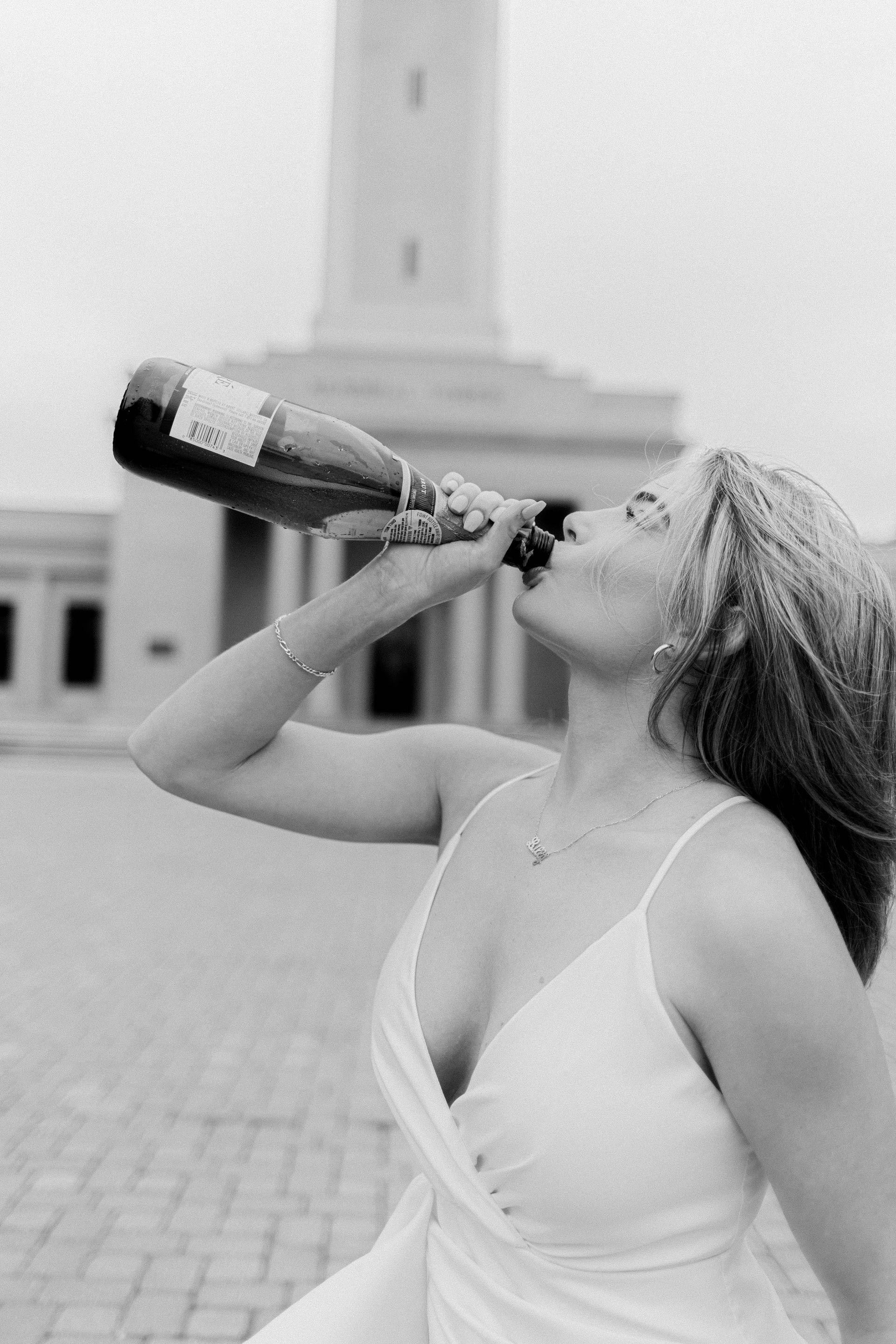 Woman in a white dress drinking from a bottle outdoors near a tall monument