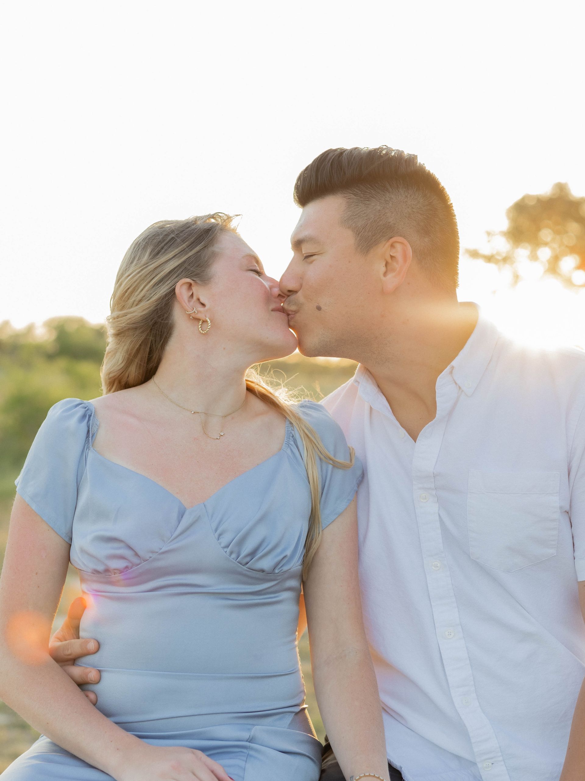 Couple kissing outdoors in soft sunlight, wearing light-colored tops
