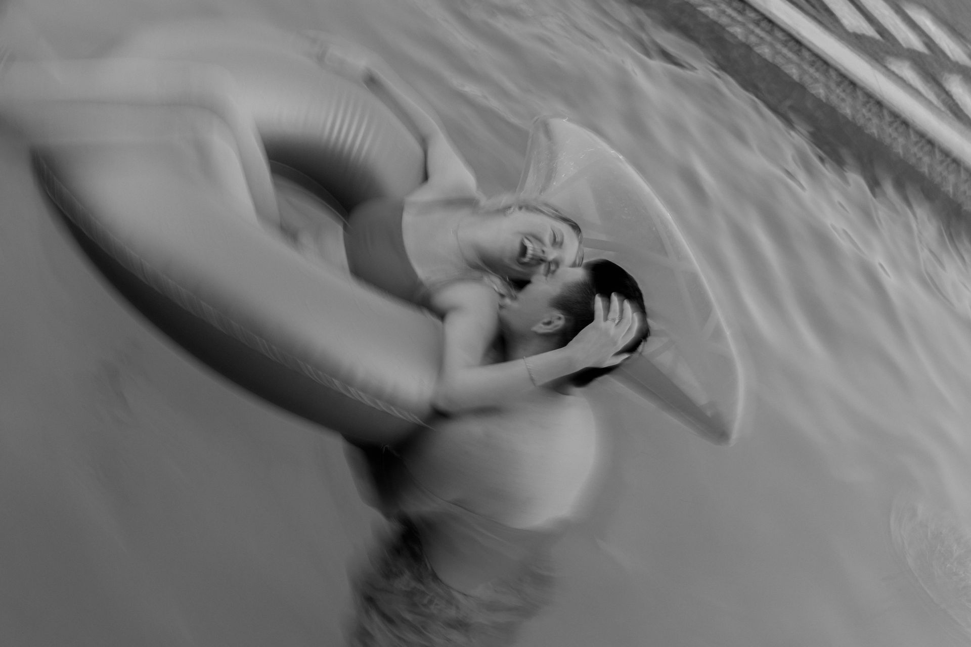 Person lounging in a striped inflatable float on water, seen in black and white