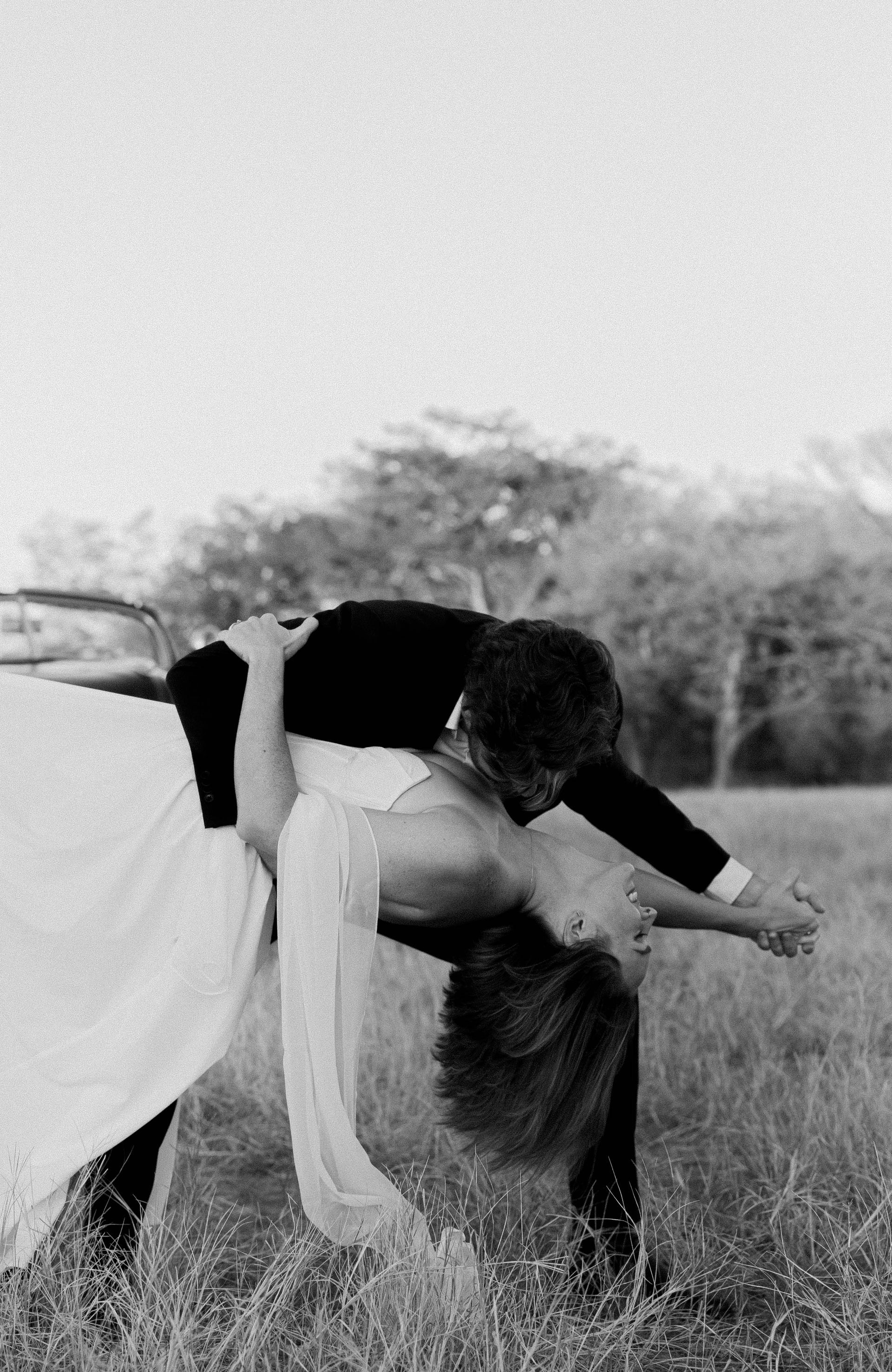 Person crouching in a grassy field, holding a large white and black dress or fabric.