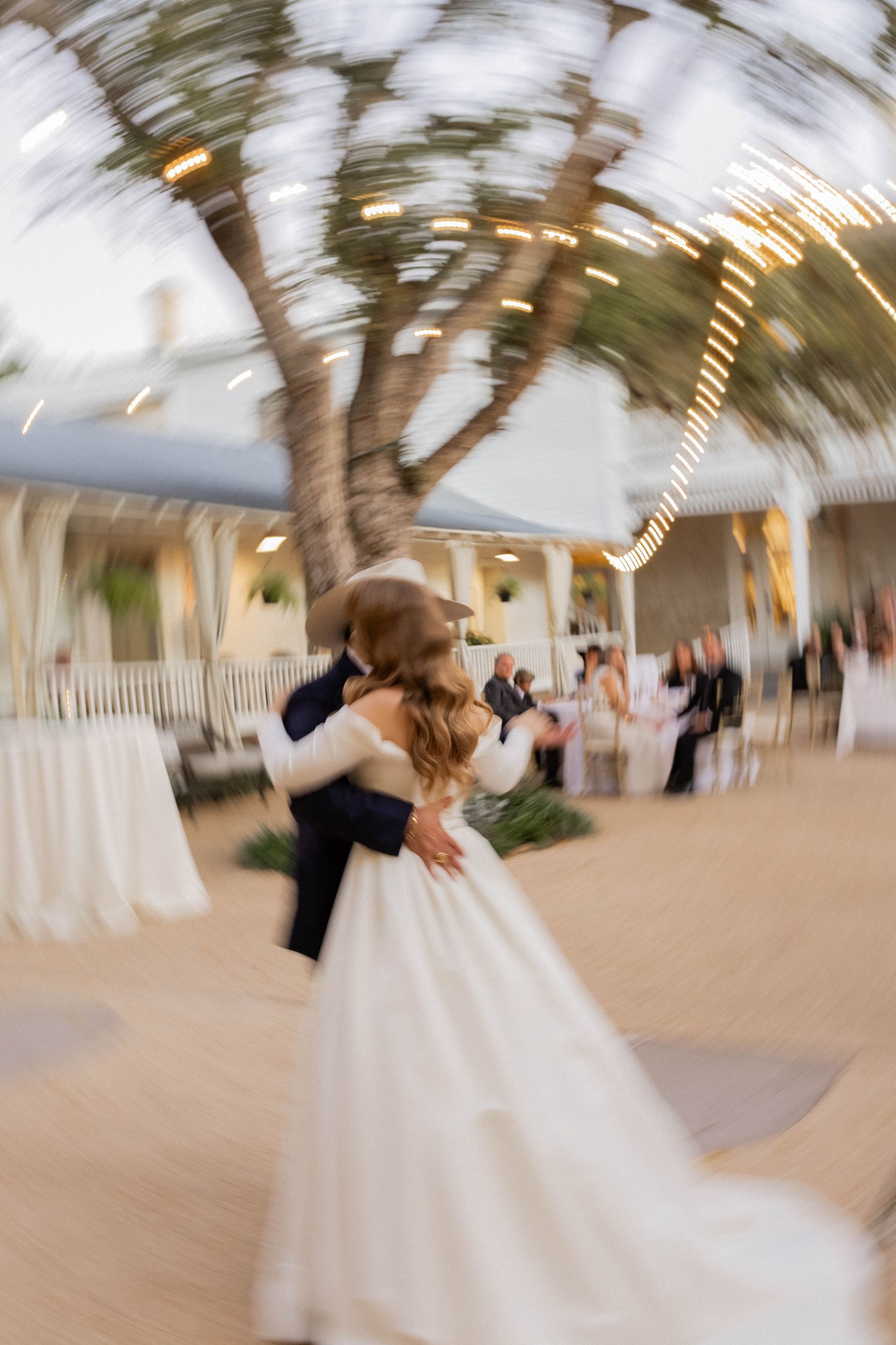 Bride and groom dancing under palm trees at an outdoor evening reception