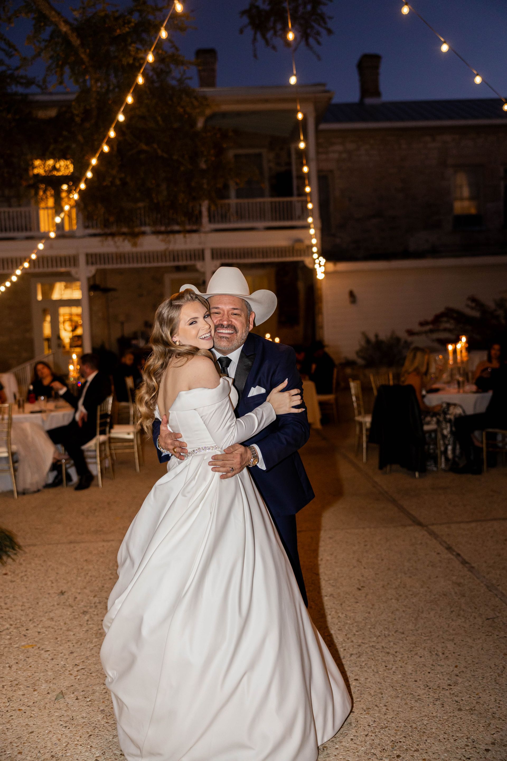 Bride and groom dancing at a nighttime outdoor wedding reception under string lights.