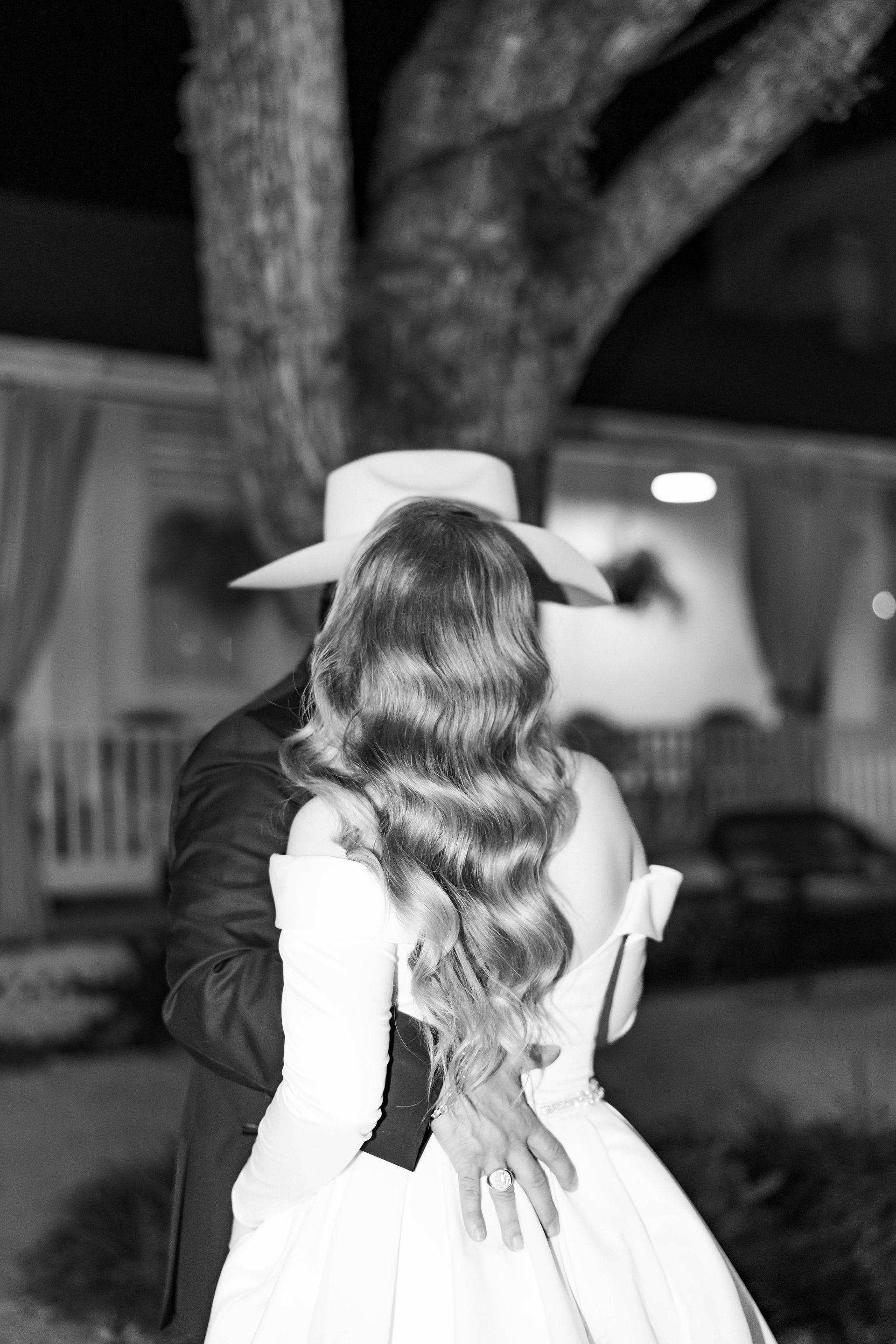 Couple embracing outdoors at night near a tree, with the woman’s long wavy hair visible from behind